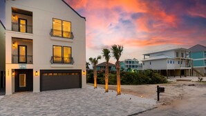Un immeuble résidentiel moderne à plusieurs étages, doté d’un garage, d’une allée et d’une pelouse bien entretenue agrémentée de palmiers.