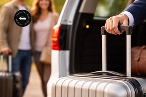 Eine Person zieht einen Koffer aus dem Kofferraum eines Fahrzeugs.