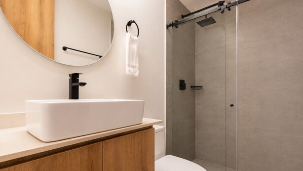 A bathroom with a white sink, a round mirror, a towel rack, a toilet, and a glass shower enclosure.