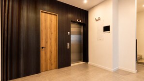 Un pasillo con puerta de madera, un ascensor y una lámpara fijada a la pared.