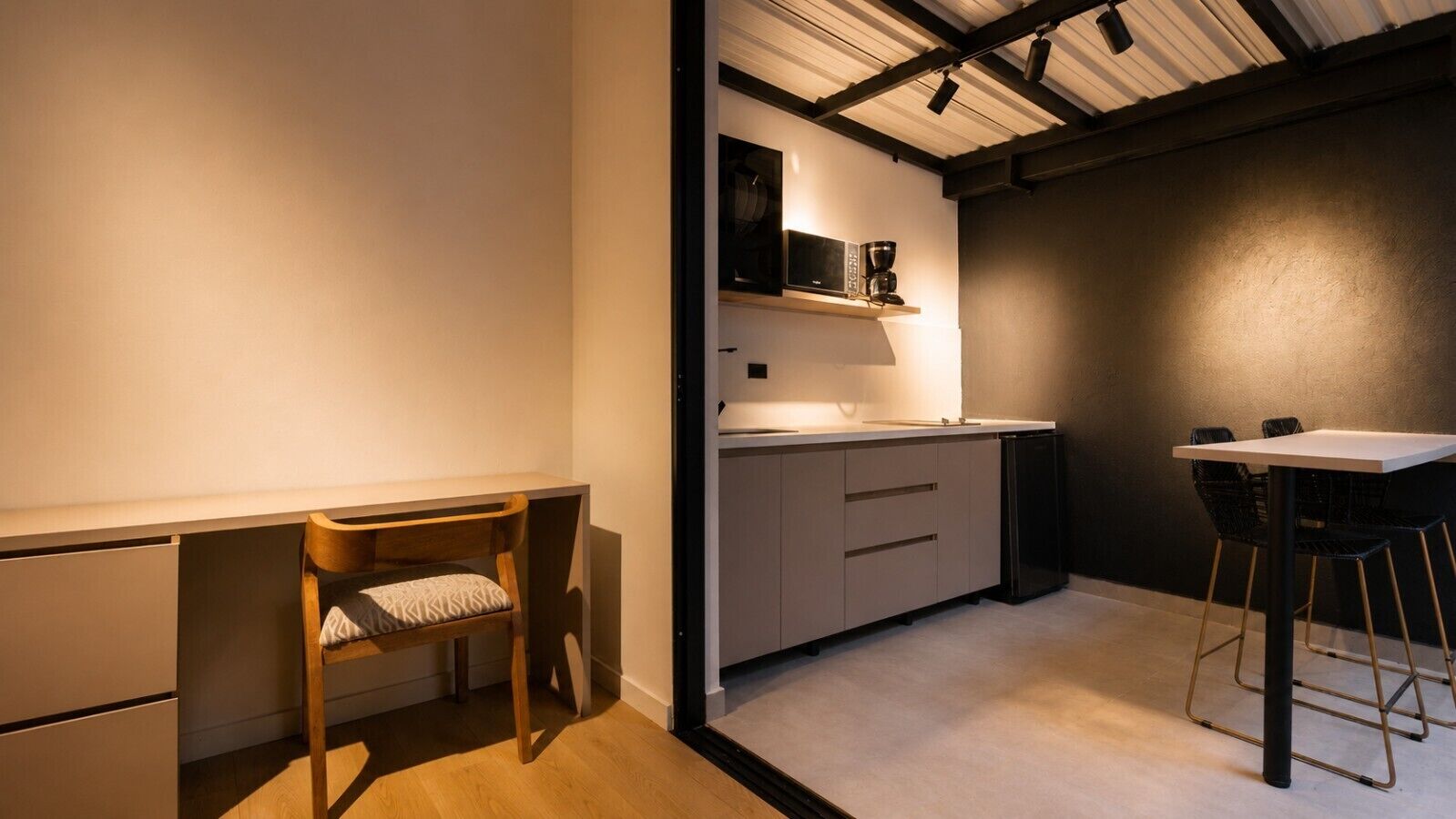 Una cocina funcional con una silla de madera, una mesita y un microondas en un estante.