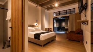 Un dormitorio con cama, piso de madera, escritorio y una silla.