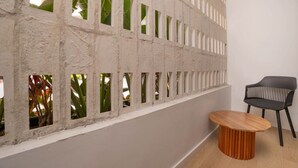 Une pièce avec une cloison en béton percée de petites fenêtres, une table ronde en bois et une chaise noire.
