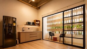 Une cuisine moderne équipée d’un réfrigérateur, d’un four à micro-ondes et d’une machine à café sur le plan de travail. Une porte-fenêtre coulissante offre une vue sur la verdure à l’extérieur.
