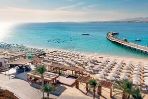 A beach resort with sun umbrellas, lounge chairs, and a pier extending into the sea. - SRNTY Sahl Hasheesh (Sahl Hasheeh)