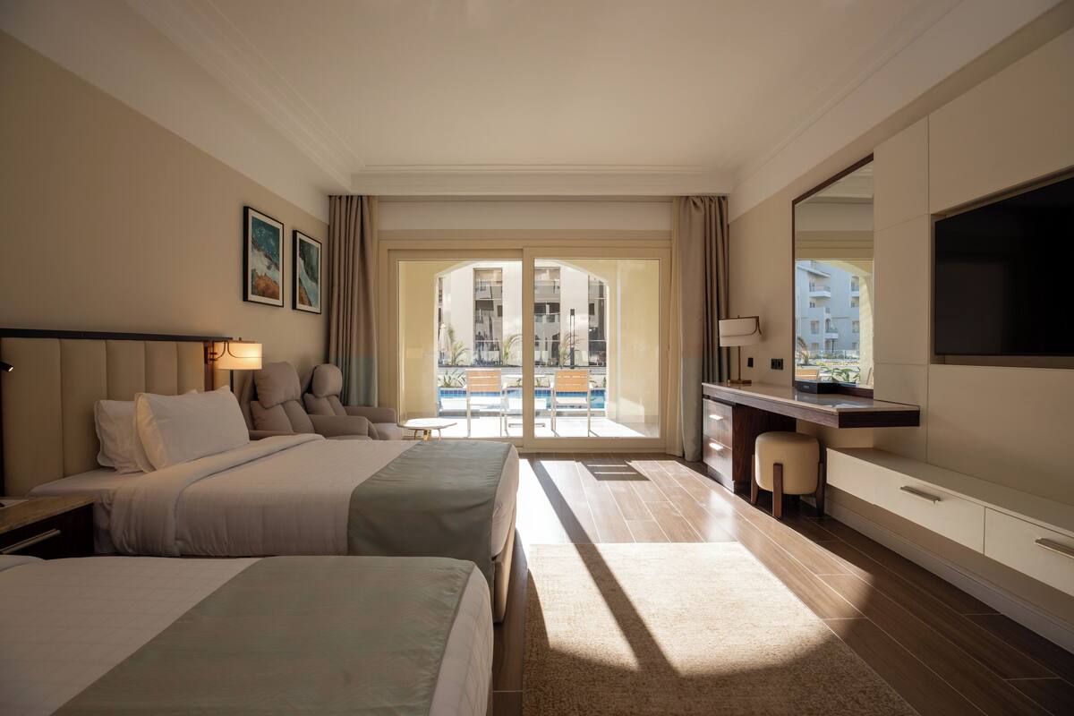 A hotel room with a bed, a desk, a chair, a TV, and a balcony with a pool view.