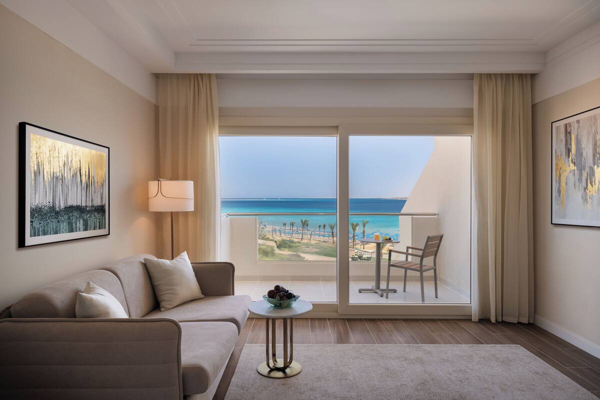 A modern hotel room with a balcony, a sofa, a table with fruit, and a lamp.