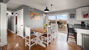 Une cuisine moderne avec une table et des chaises en bois, un luminaire suspendu et une vue sur l’extérieur.