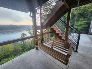 Un escalier en bois, doté d’une rampe métallique, surplombe une rivière et une végétation luxuriante.