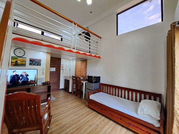 A compact room with a bunk bed, a desk with a computer, a TV, and a small kitchenette.