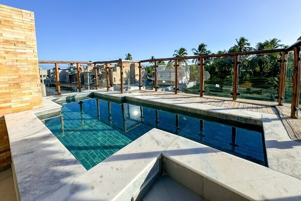 A rooftop swimming pool with a clear blue water feature, surrounded by a wooden pergola and a brick wall.