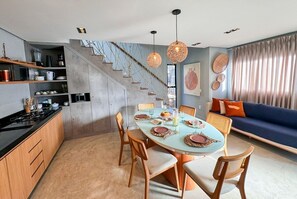 A modern kitchen with a dining area, a staircase, and a living room with a sofa and curtains.