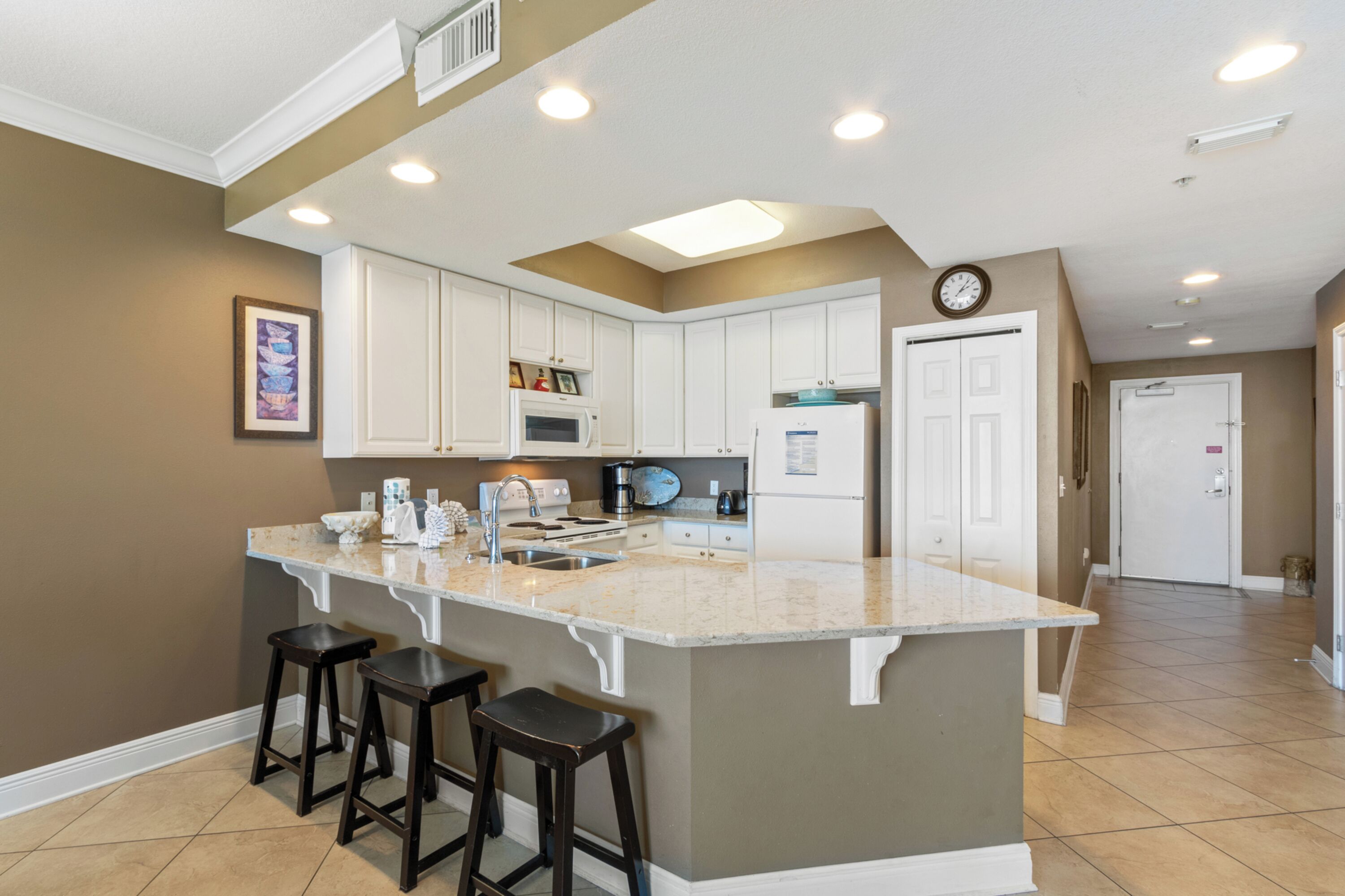 A kitchen with white cabinets, a central island with stools, a microwave, and a refrigerator.