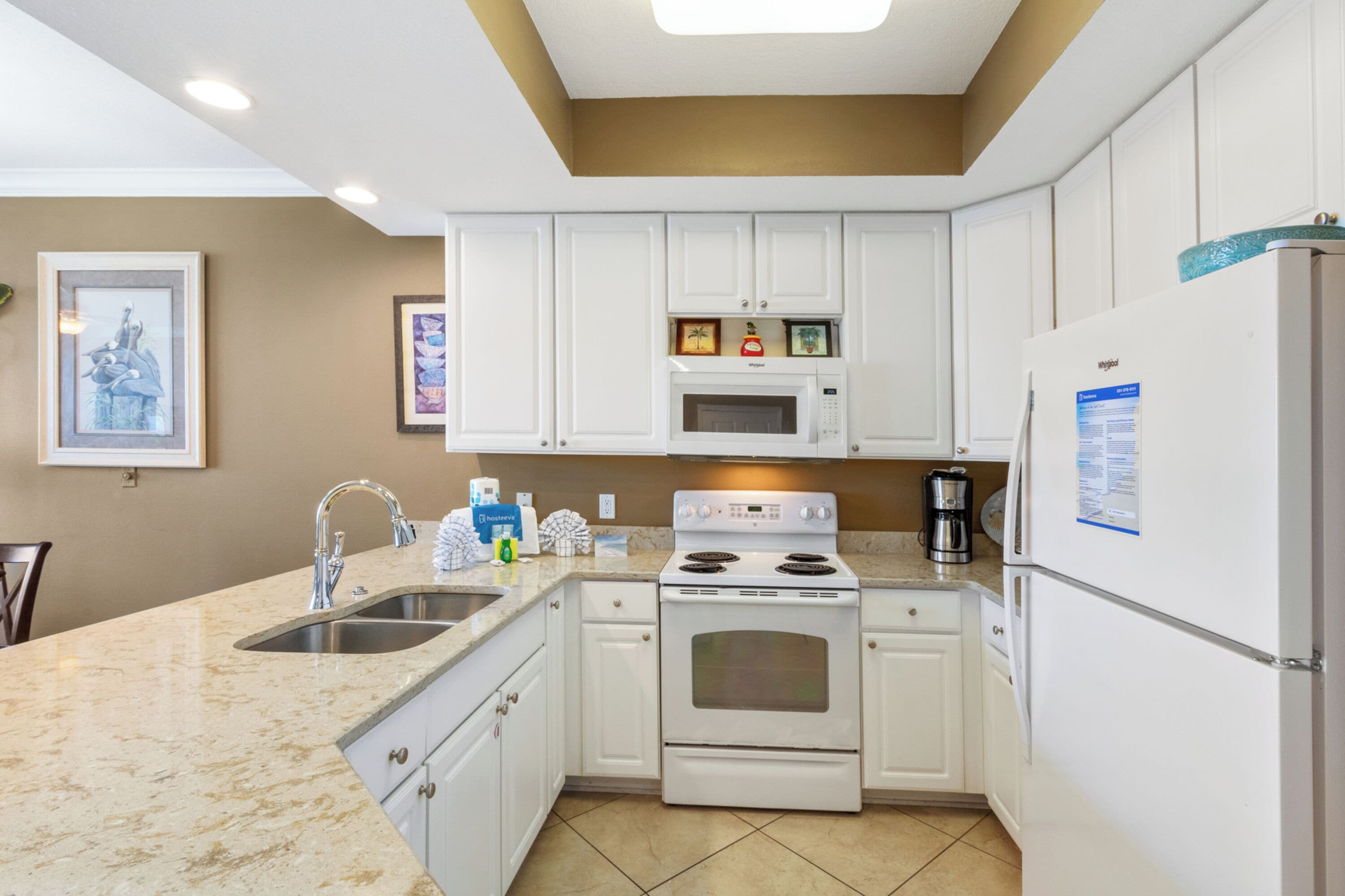 A kitchen with white cabinets, a stainless steel sink, a microwave, an oven, and a refrigerator.