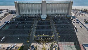 Un gran hotel con un patio central, varios estacionamientos y vistas al océano.