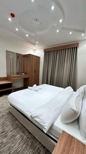 Une chambre d’hôtel avec un grand lit, un bureau en bois, un miroir et une fenêtre avec des rideaux.