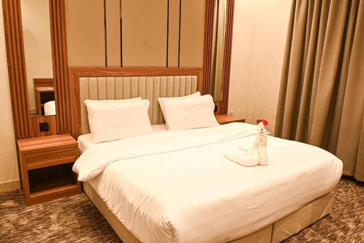 A neatly made bed with white linens, a wooden headboard, and a nightstand with a lamp.