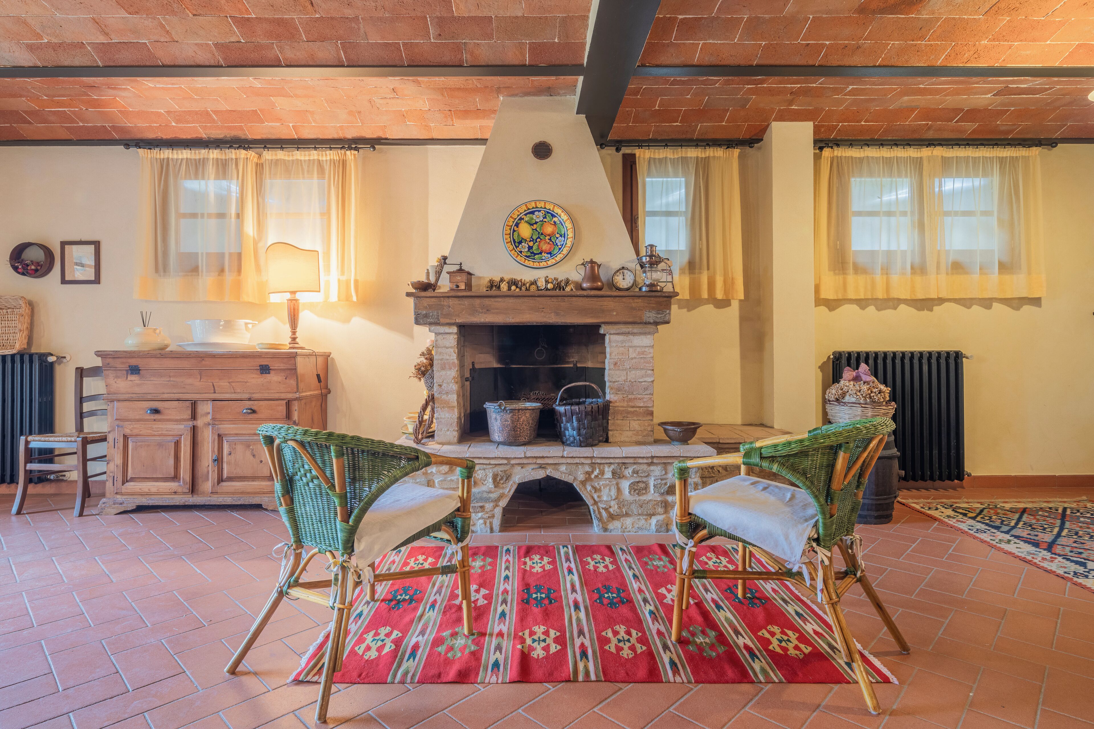 Una sala de estar acogedora con chimenea de piedra, sillones de mimbre y piso de baldosas.