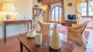 A cozy living room with a wooden table, wicker chairs, a TV, and a fireplace. - Casa Viola Pool Wifi Montaione (Montaione)