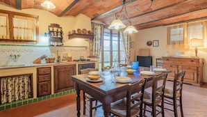 A rustic kitchen with a wooden table set for dining, a brick ceiling, and a window with curtains. - Casa Viola Pool Wifi Montaione (Montaione)