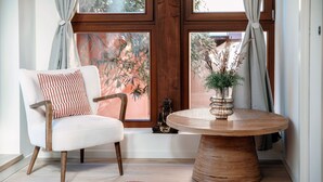 Una habitación con un sillón blanco, una mesa redonda de madera y una ventana con cortinas.