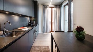 Una cocina moderna con armarios oscuros, un lavamanos de acero inoxidable y una zona de comedor con una mesa y un jarrón de flores.