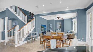 A spacious living area with a dining table, chairs, and a staircase leading to an upper floor.