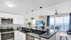 A modern kitchen with a central island, stainless steel appliances, and a view to a balcony with a scenic ocean backdrop.