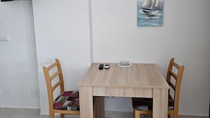 En matplats med ett träbord och två stolar, en målning av en segelbåt på väggen och en platt-TV som är monterad på väggen.