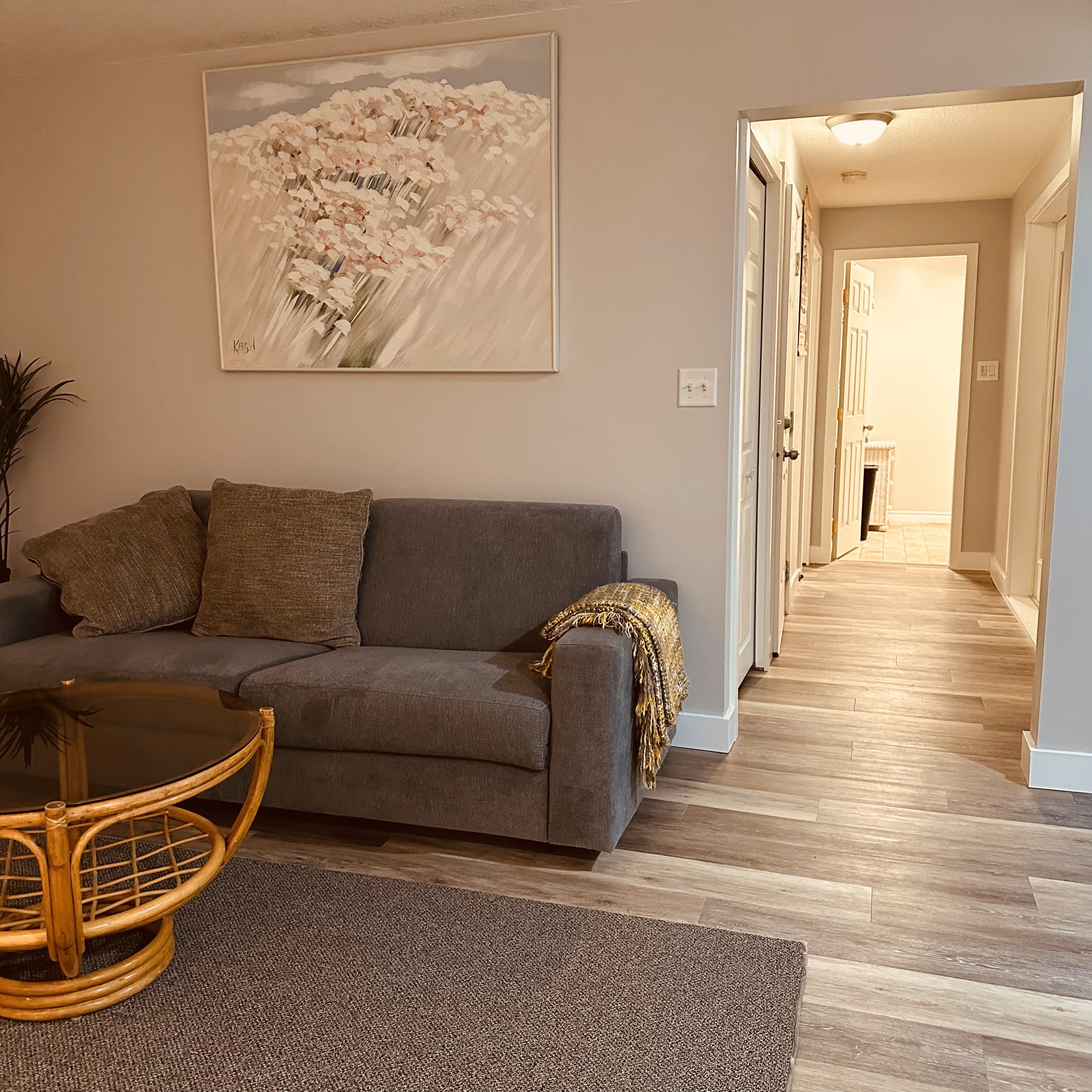 Un salon avec un canapé gris, une table basse ronde en bois et un grand tableau abstrait accroché au mur.