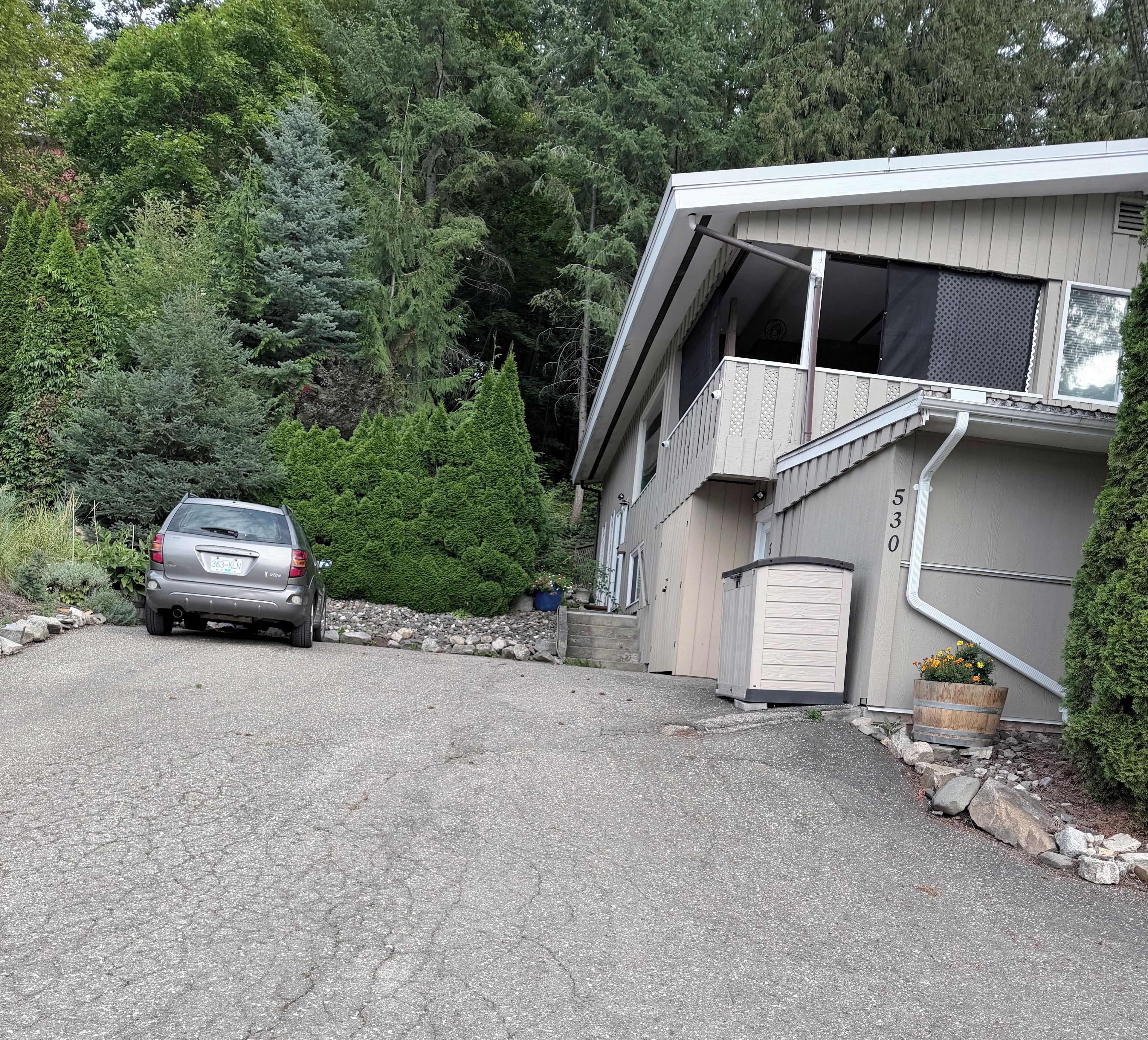 A residential driveway leading to a house with a garage, surrounded by dense greenery and trees.