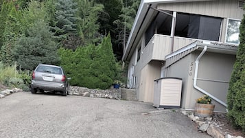 A residential driveway leading to a house with a garage, surrounded by dense greenery and trees.