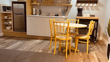 A compact kitchen with a refrigerator, microwave, and coffee maker. There is a dining table with chairs and a rug on the floor.