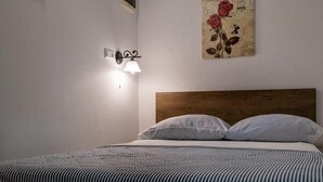 Ein Schlafzimmer mit einem hölzernen Kopfende, einem Einzelbett mit weißer Bettwäsche, einer Wandleuchte und einem floralen Bild an der Wand.