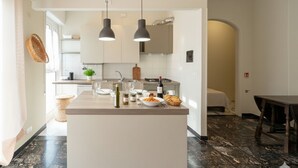 A modern kitchen with a central island, pendant lights, and a dining area with a table and chairs. - Cycling Riviera apartment (Imperia)