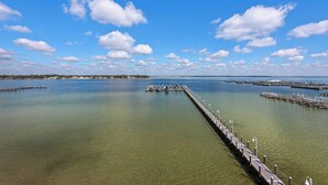 Une jetée s’avançant dans une étendue d’eau calme, sous un ciel dégagé parsemé de quelques nuages.