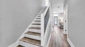 A staircase with wooden steps and white walls, leading to a door with a view of greenery outside. - ☀️4 Bikes-30A-Under the Oaks Cottage in Blue Mountain Beach☀️ (Santa Rosa Beach)