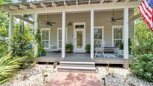 A two-story house with a covered porch, a flag, and a patio with seating. - ☀️4 Bikes-30A-Under the Oaks Cottage in Blue Mountain Beach☀️ (Santa Rosa Beach)