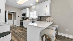 A modern kitchen with white cabinetry, a central island, pendant lighting, and a wooden floor. - ☀️4 Bikes-30A-Under the Oaks Cottage in Blue Mountain Beach☀️ (Santa Rosa Beach)
