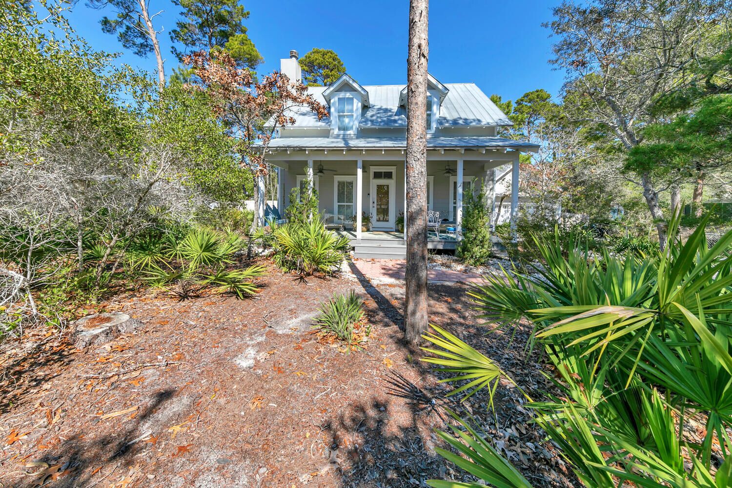 A two-story house with a covered porch, surrounded by various plants and trees.