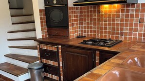 A kitchen with a built-in oven, a gas stove, and a black range hood. There is a wooden cabinet with a clock and a vase on top.