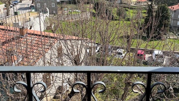 A balcony with a wrought iron railing overlooking a residential area with houses and a mountainous backdrop.