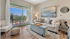 A modern living room with a sofa, ottoman, and a dining area with chairs. - ☀️30A Private Beach Access-Pool-Inn at Seacrest 309- Somewhere in the Sun☀️ (Inlet Beach)