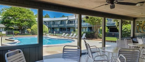 A covered outdoor area with a pool, lounge chairs, and tables.