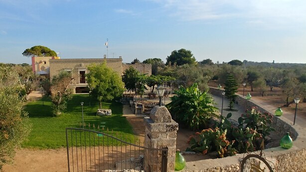 A courtyard with a stone gate, a small building, and a garden with various plants and a pergola. - Luxury studio apartment in farmhouse (Sannicola)