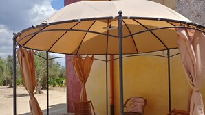 A covered outdoor seating area with two wooden chairs and a table, surrounded by a metal frame and beige curtains. - Luxury studio apartment in farmhouse (Sannicola)