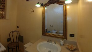 A bathroom with a large mirror, two wall-mounted lights, a sink, and a chair. - Luxury studio apartment in farmhouse (Sannicola)