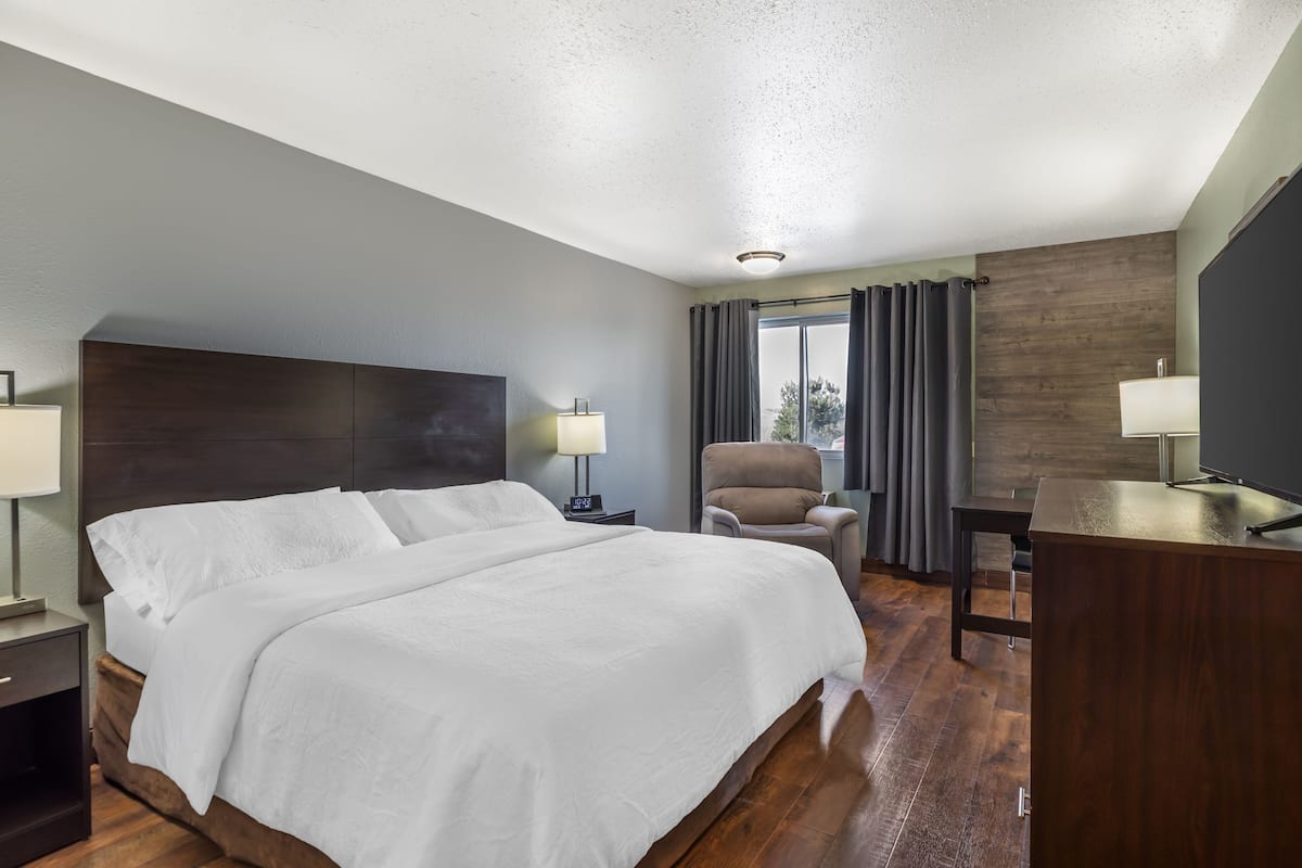 A hotel room with a large bed, a desk, a chair, and a TV.