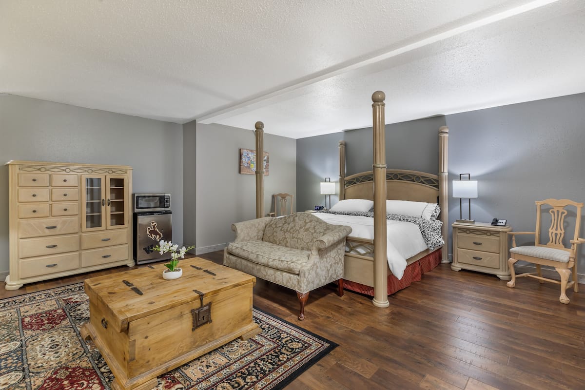 A bedroom with a four-poster bed, a wooden chest, a sofa, a nightstand, and a chair.
