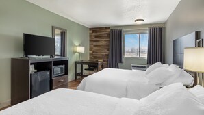 Een hotelkamer met twee bedden, een bureau, een televisie en een raam met gordijnen.